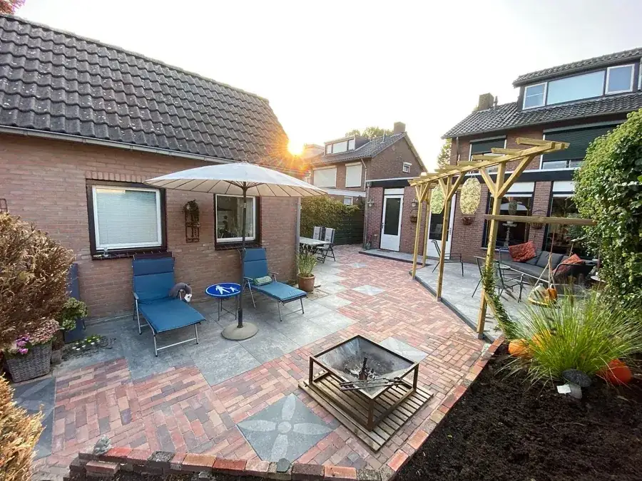 Een achtertuin met bestrating, beplanting en een houten pergola. Het terras biedt ruimte om buiten te zitten.