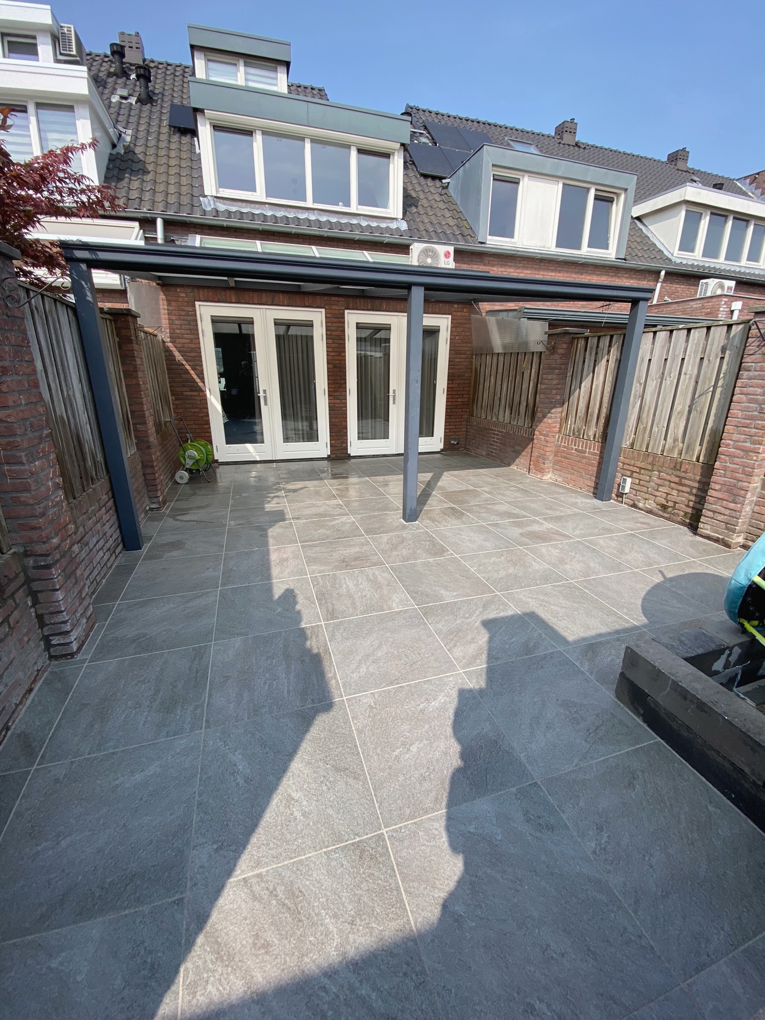 Een ruim betegeld terras onder een overkapping aan huis.