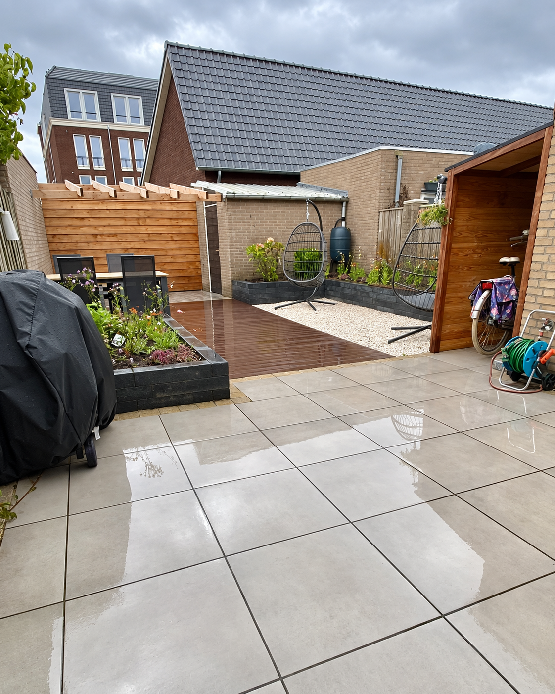 Een houten terras met plantenbakken, siergrind en een fijne hoek om te zitten.