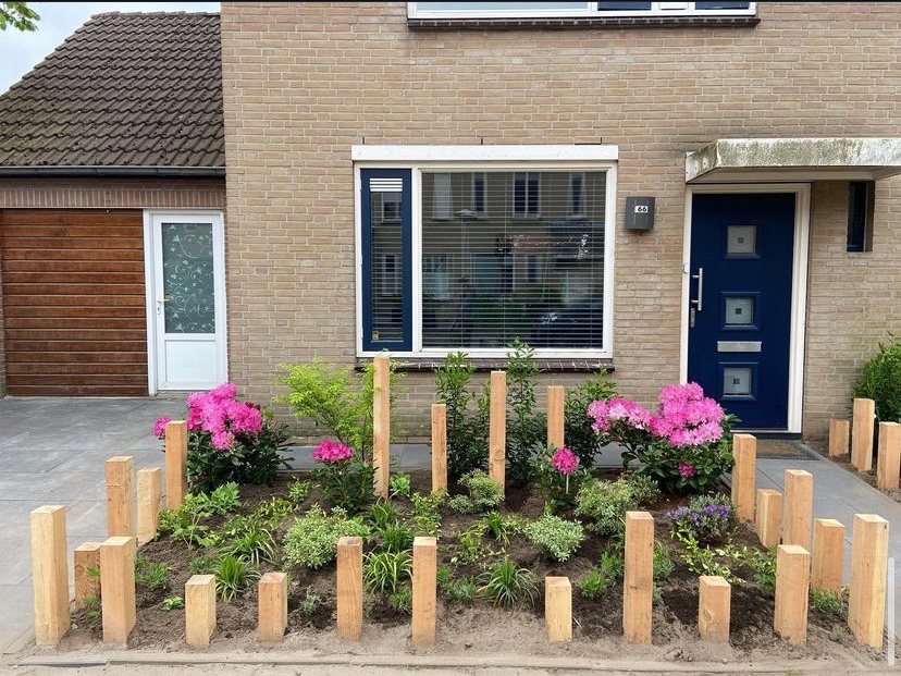 Een beplante voortuin met bloeiende struiken, siergrassen en houten paaltjes.