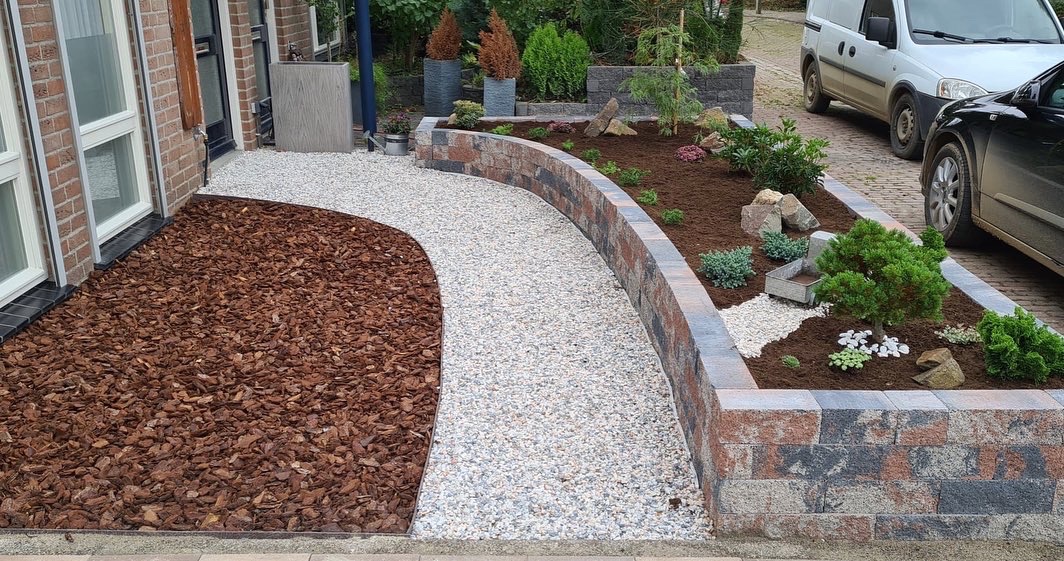 Een voortuin met een gebogen pad van siergrind, lage muurtjes en beplanting.