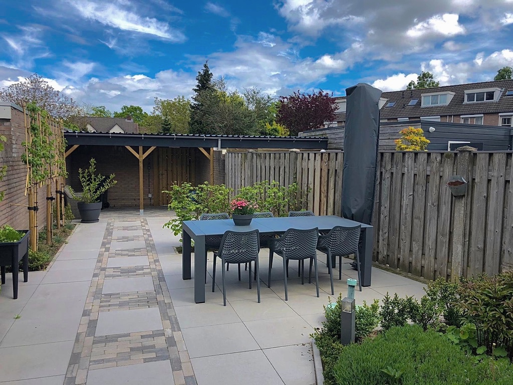 Een tuin met een terras, een eethoek en beplanting rondom.